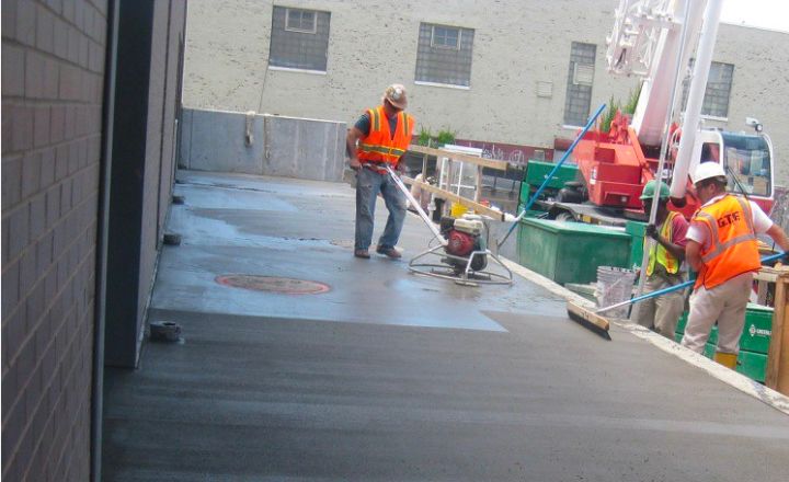 Two men in orange vests finishing a concrete sidewalk